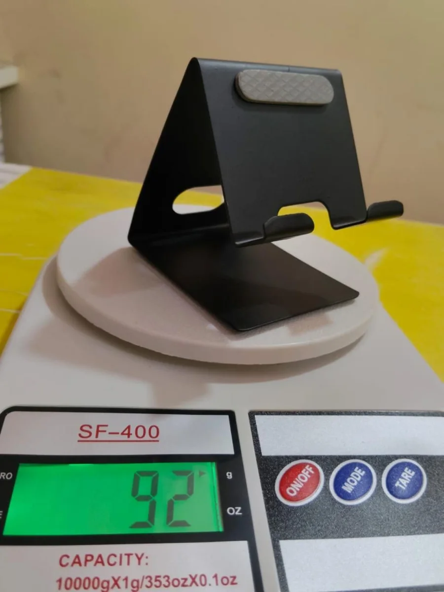 Black folded-metal stand that holds a phone upright on a desk, with a grip pad