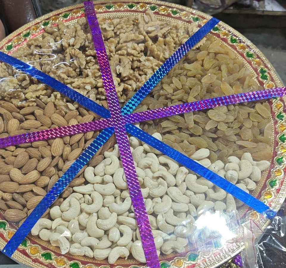 A round platter with a painted red, green and gold rim, filled with almonds, cashews, golden raisins and walnuts, under…
